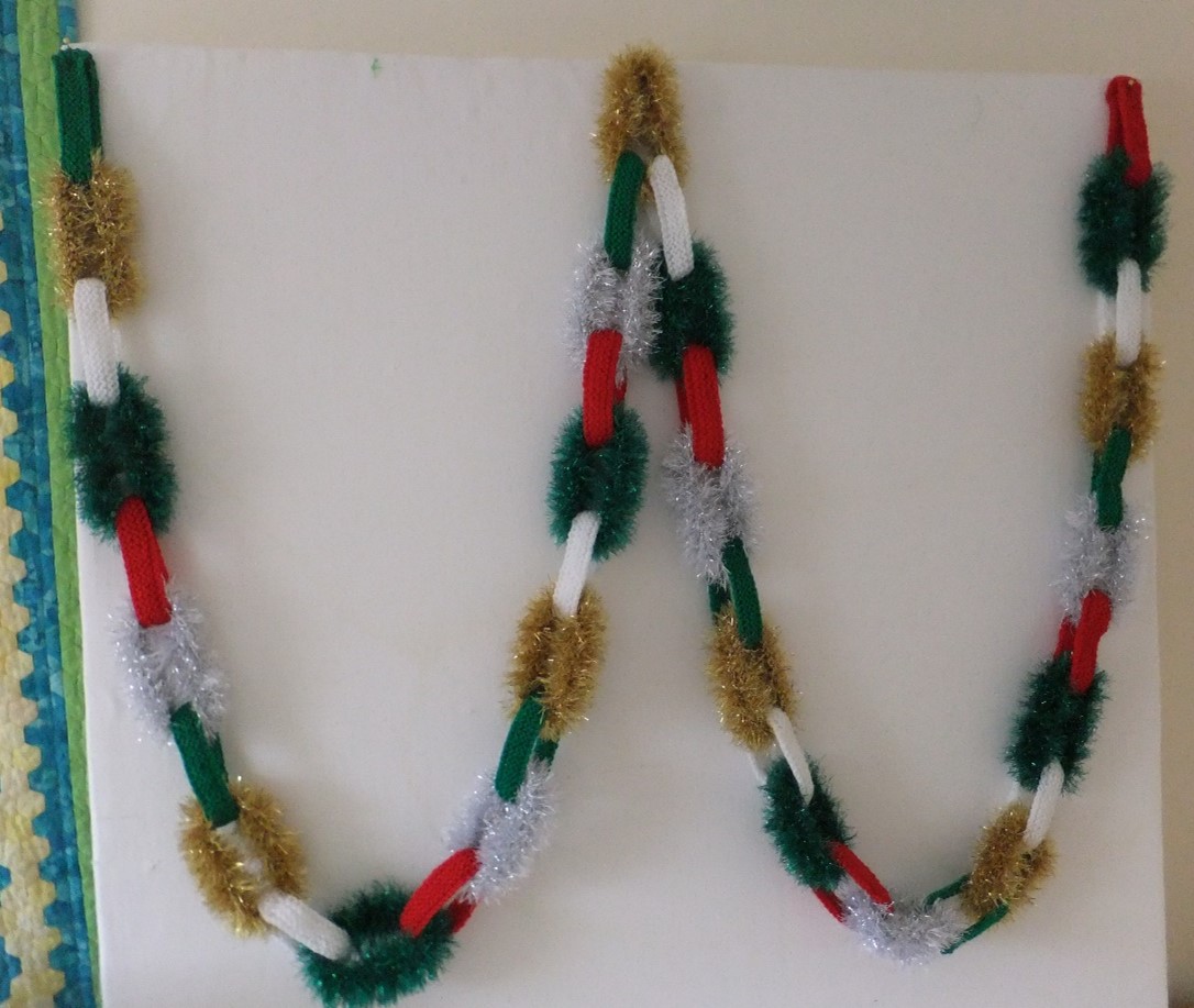 a long chain of knitted loops in Red, Green, White, gold tinsel, silver tinsel and green tinsel